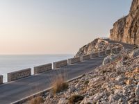 the empty highway on the side of a cliff in the sunset overlooking a body of water