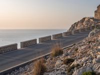 the empty highway on the side of a cliff in the sunset overlooking a body of water