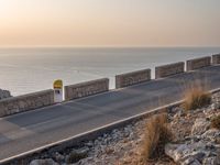 the empty highway on the side of a cliff in the sunset overlooking a body of water