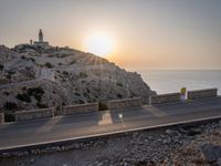 the empty highway on the side of a cliff in the sunset overlooking a body of water