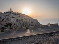 the empty highway on the side of a cliff in the sunset overlooking a body of water