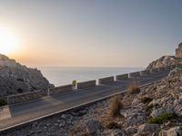 the empty highway on the side of a cliff in the sunset overlooking a body of water