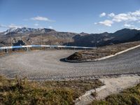 a graveled area with a curved path and blue railing on top of it with the snowy mountains in the distance