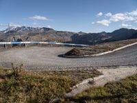 a graveled area with a curved path and blue railing on top of it with the snowy mountains in the distance