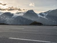 a car parked on a parking lot with snow covered mountains in the background with clouds