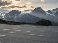 a car parked on a parking lot with snow covered mountains in the background with clouds