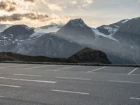 a car parked on a parking lot with snow covered mountains in the background with clouds