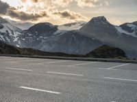 a car parked on a parking lot with snow covered mountains in the background with clouds