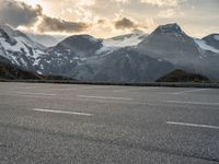 a car parked on a parking lot with snow covered mountains in the background with clouds