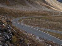 a road near mountains that has a car driving down it, with cloudy skies overhead