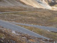 a road near mountains that has a car driving down it, with cloudy skies overhead