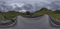 the fisheye view of a curve on a road with mountains in the background and a small red umbrella on top of the curb