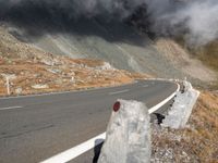 a motorcycle traveling on the road in a mountainside area, with a dark smoke filled sky