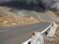 a motorcycle traveling on the road in a mountainside area, with a dark smoke filled sky