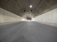 a street is surrounded by a dark tunnel with light from behind it, and only one lane has lanes