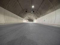 a street is surrounded by a dark tunnel with light from behind it, and only one lane has lanes