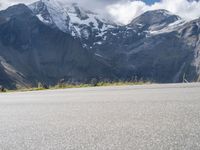 a person is standing on the road watching mountains go by and snow covered mountains in the distance