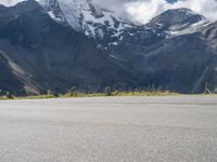 a person is standing on the road watching mountains go by and snow covered mountains in the distance