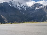 a person is standing on the road watching mountains go by and snow covered mountains in the distance