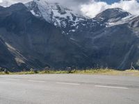 a person is standing on the road watching mountains go by and snow covered mountains in the distance