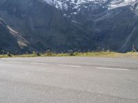 a person is standing on the road watching mountains go by and snow covered mountains in the distance