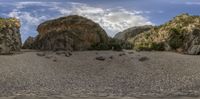 two rocks surrounded by trees and a lake in the sand with clouds above them on the blue sky