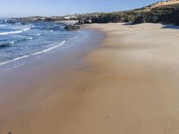 a lone beach with waves coming in towards the shore and sandy coastline under a clear sky