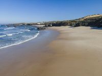 a lone beach with waves coming in towards the shore and sandy coastline under a clear sky