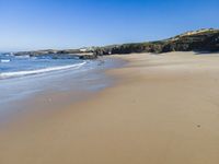 a lone beach with waves coming in towards the shore and sandy coastline under a clear sky