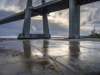 a concrete paved sidewalk with a very large bridge in the background overcast sky and water