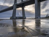 a concrete paved sidewalk with a very large bridge in the background overcast sky and water