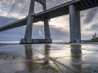 a concrete paved sidewalk with a very large bridge in the background overcast sky and water