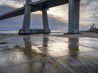 a concrete paved sidewalk with a very large bridge in the background overcast sky and water