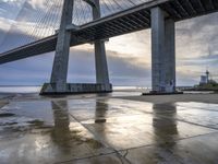 a concrete paved sidewalk with a very large bridge in the background overcast sky and water