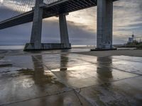 a concrete paved sidewalk with a very large bridge in the background overcast sky and water