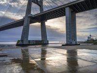 a concrete paved sidewalk with a very large bridge in the background overcast sky and water