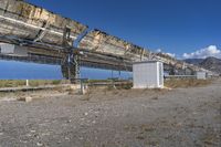 an industrial structure with large solar panels in a desert field near the ocean, along with a bench to watch for fish