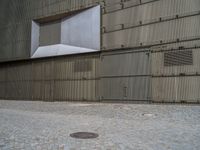 a city fire hydrant in front of a brick sidewalk next to a building, which looks like a metal warehouse