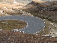 a mountain road curves very fast along the mountainside near to snow capped peaks and rocky fields