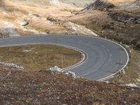 a mountain road curves very fast along the mountainside near to snow capped peaks and rocky fields