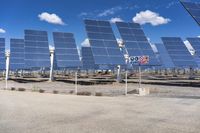 a row of solar panels, sitting on a gravel area, with a sign in front