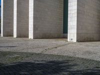 a large building with several columns on the top and bottom of the building, two people sitting on a sidewalk and one standing