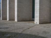 a large building with several columns on the top and bottom of the building, two people sitting on a sidewalk and one standing