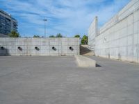 the empty parking lot in front of a wall with apartment buildings on it and a skateboarder on a ramp