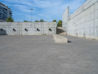 the empty parking lot in front of a wall with apartment buildings on it and a skateboarder on a ramp