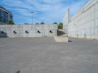 the empty parking lot in front of a wall with apartment buildings on it and a skateboarder on a ramp