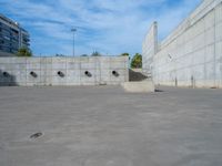 the empty parking lot in front of a wall with apartment buildings on it and a skateboarder on a ramp