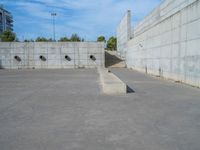 the empty parking lot in front of a wall with apartment buildings on it and a skateboarder on a ramp