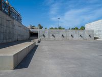 the empty parking lot in front of a wall with apartment buildings on it and a skateboarder on a ramp