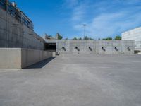 the empty parking lot in front of a wall with apartment buildings on it and a skateboarder on a ramp